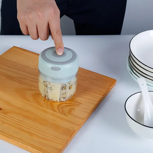 Hand pressing a button on a small kitchen appliance with food inside, on a wooden cutting board.